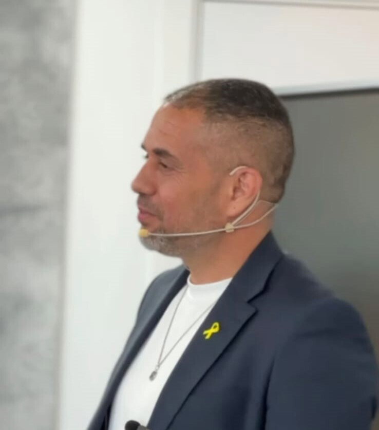 מיקי לוגסי מרצה על במה עם מיקרופון צמוד